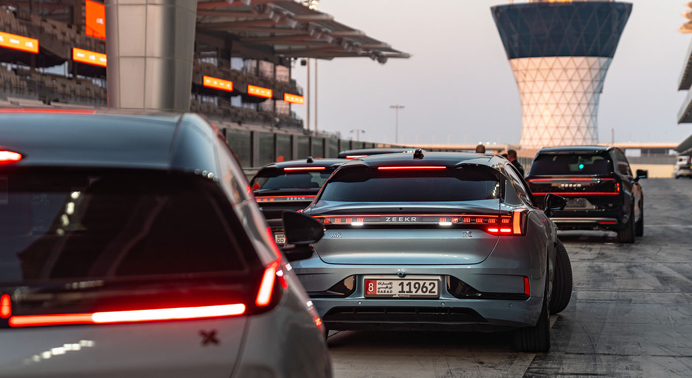 Rear view of a grey Zeekr electric sedan and other vehicles with glowing red LED taillights on a night track.